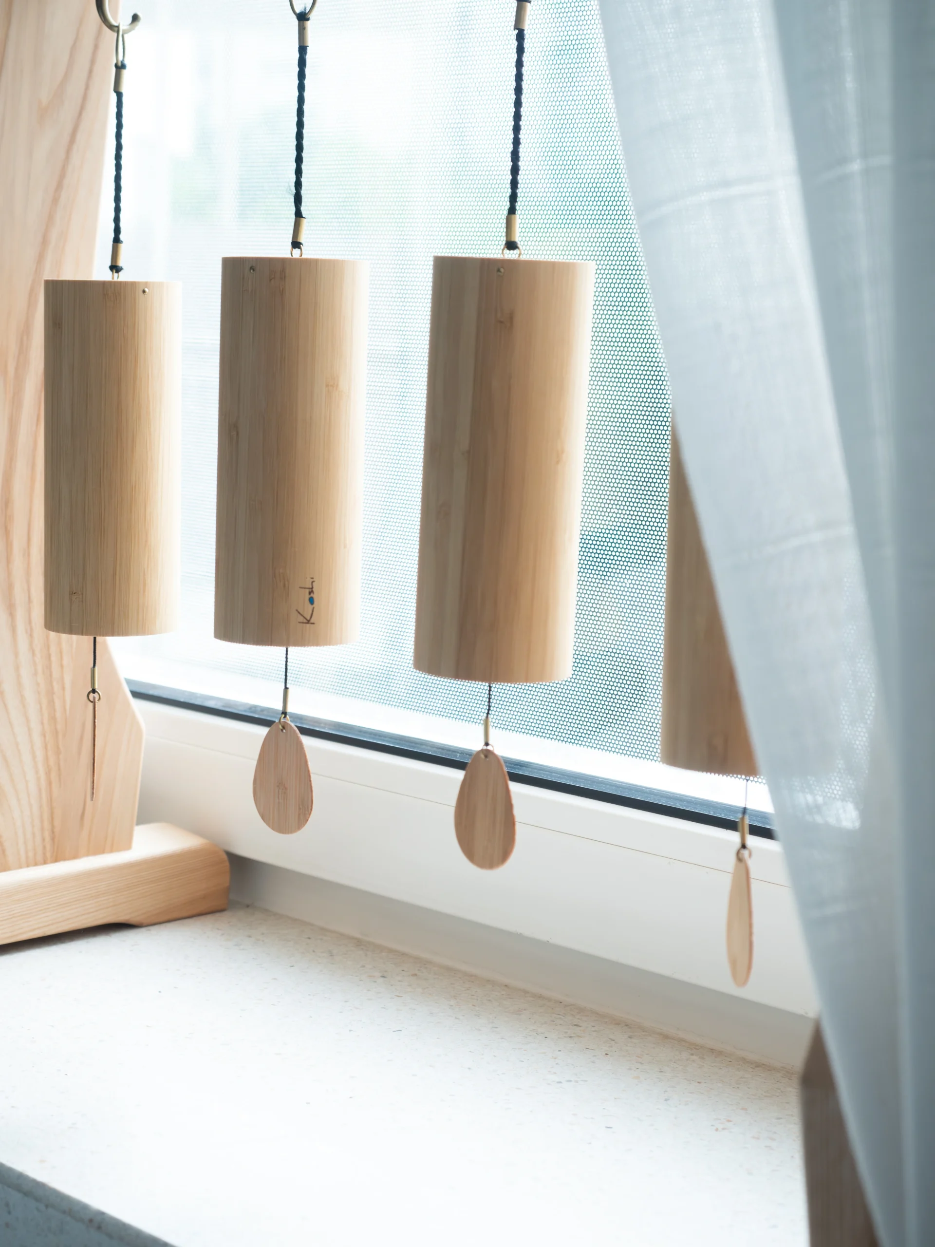Dzwonki Koshi zawieszone w oknie gabinetu, wykonane z drewna. Przedstawienie elementu wspierającego relaks i wyciszenie w przestrzeni terapeutycznej.