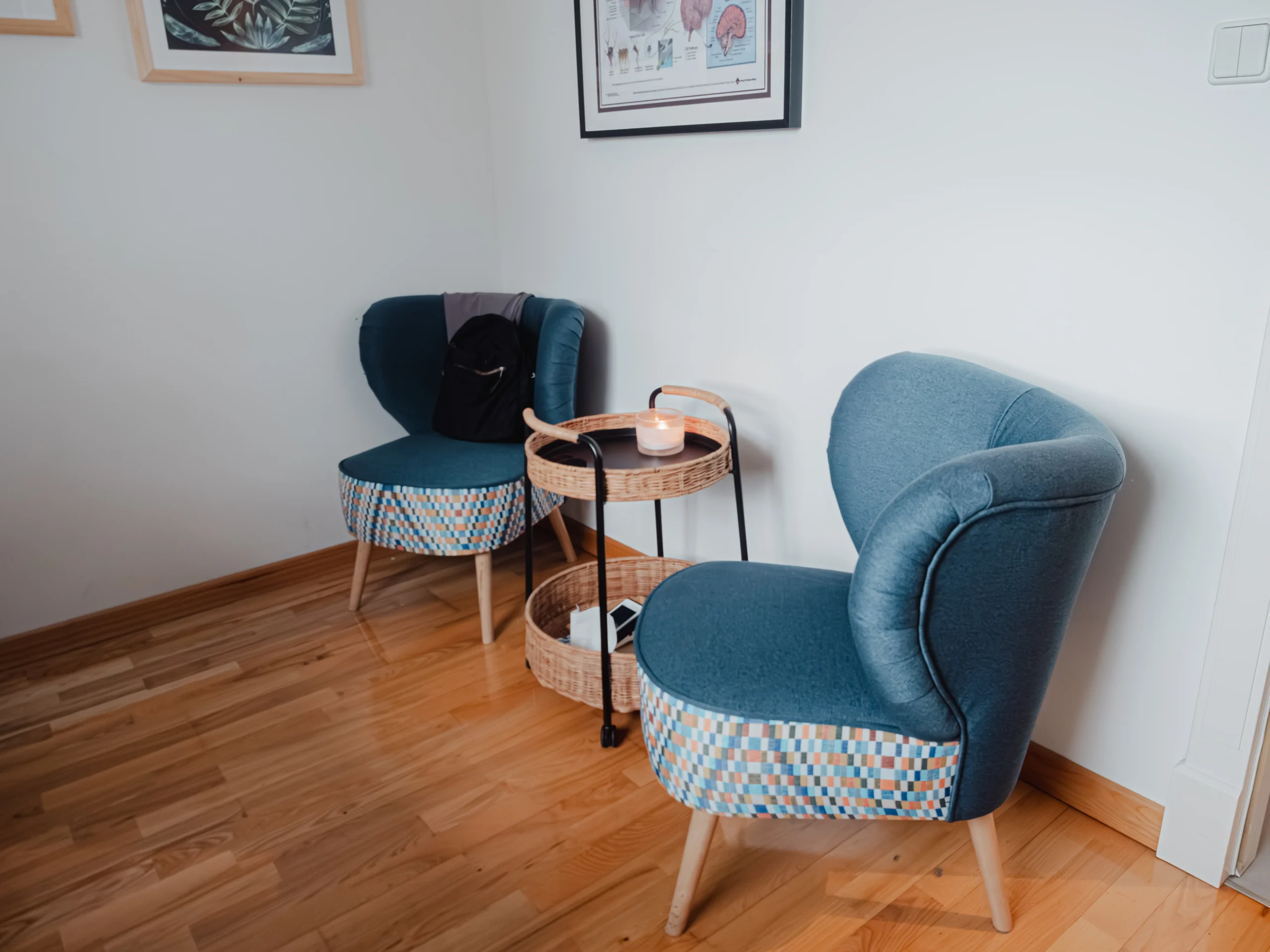Dwie niebieskie fotele, świeca i stolik w rogu gabinetu.